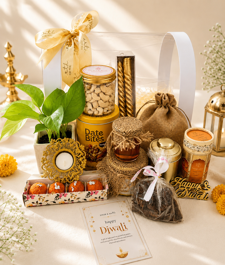Elegant Diwali gift hamper featuring assorted festive treats, cashews, candles, a decorative diya, potted plant, gift pouches, and traditional décor arranged beautifully in warm golden tones.