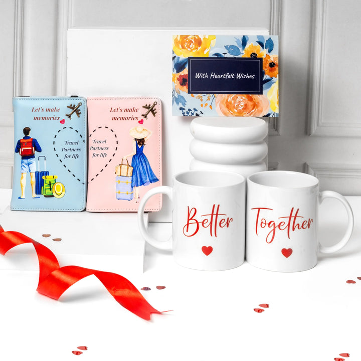 A Valentine's Day gift set featuring two white ceramic mugs with 'Better Together' in red script and heart graphics, a light blue passport holder and a pink passport holder with illustrations, a stack of three white cups, and a floral 'With Heartfelt Wishes' box, arranged on a white surface with a red ribbon. Travelling gift for Partner. Newly wed gift, Couple gift.
