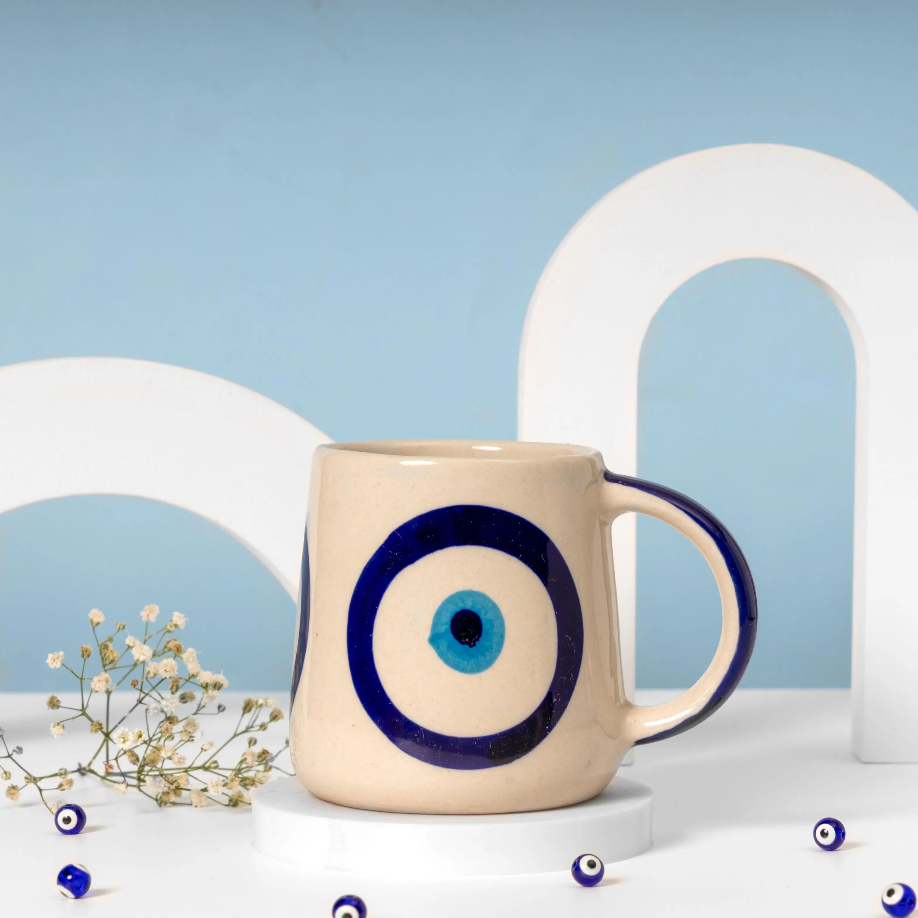 Beige mug with blue evil eye design on a white surface with a light blue background