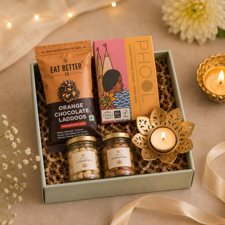 Elegant Diwali gift hamper featuring Eat Better orange chocolate ladoos, Phool incense cones, small glass jars of cashews and almonds, and a decorative lotus diya, beautifully arranged in a compact gift box.