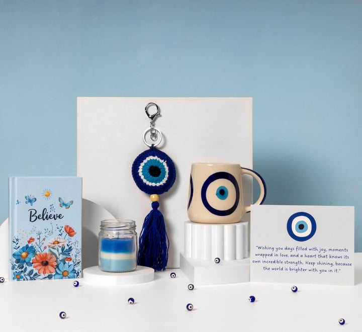 Evil Eye gift hamper featuring an evil eye mug, handcrafted evil eye keychain, scented candle, inspirational “Believe” keepsake, and heartfelt greeting card, beautifully arranged in a blue and white themed display.