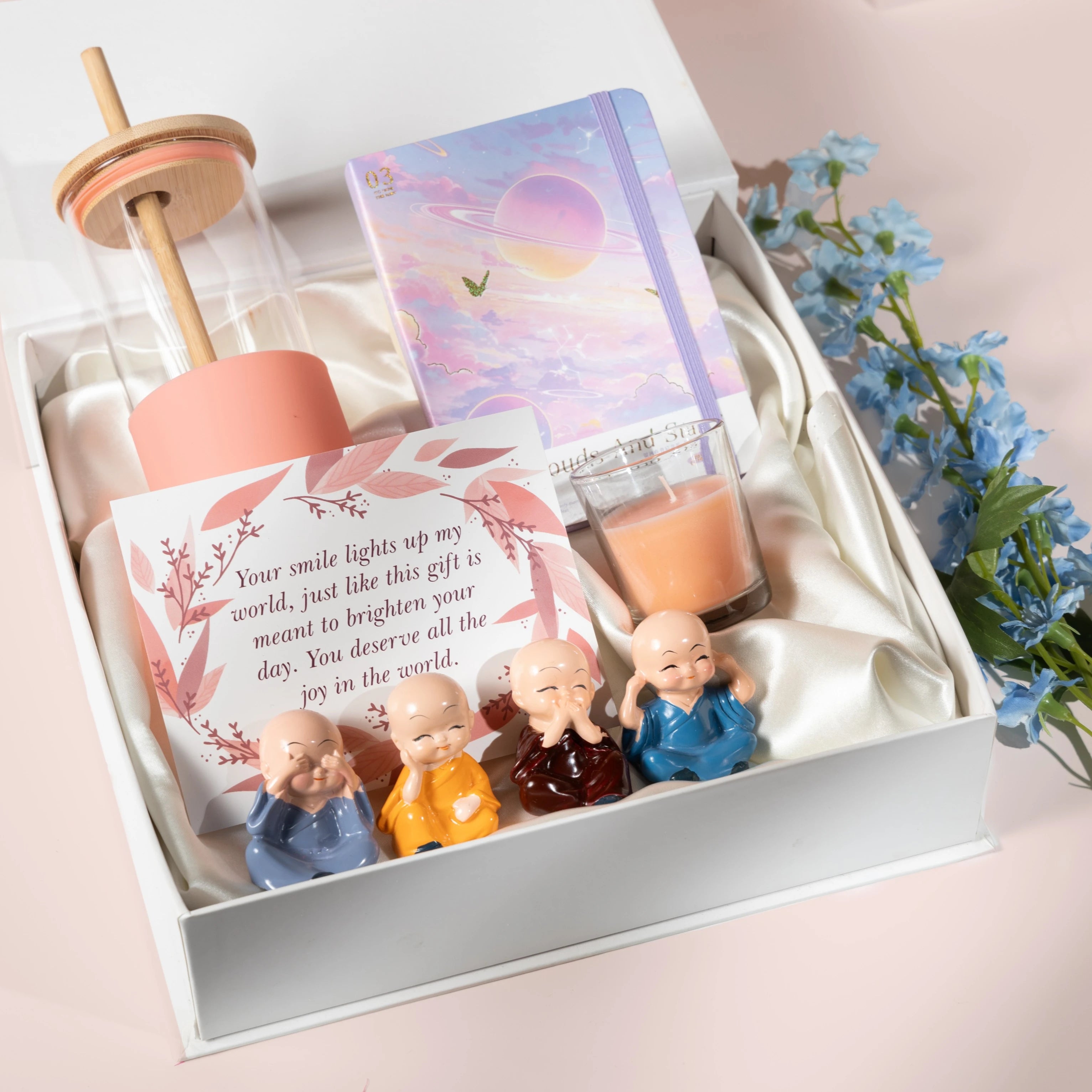 Rarejoy self-care gift hamper featuring a glass sipper bottle, aesthetic diary, scented candle, greeting card, and four monk figurines in a premium white gift box – perfect gift for women, friends, birthdays, and special occasions.