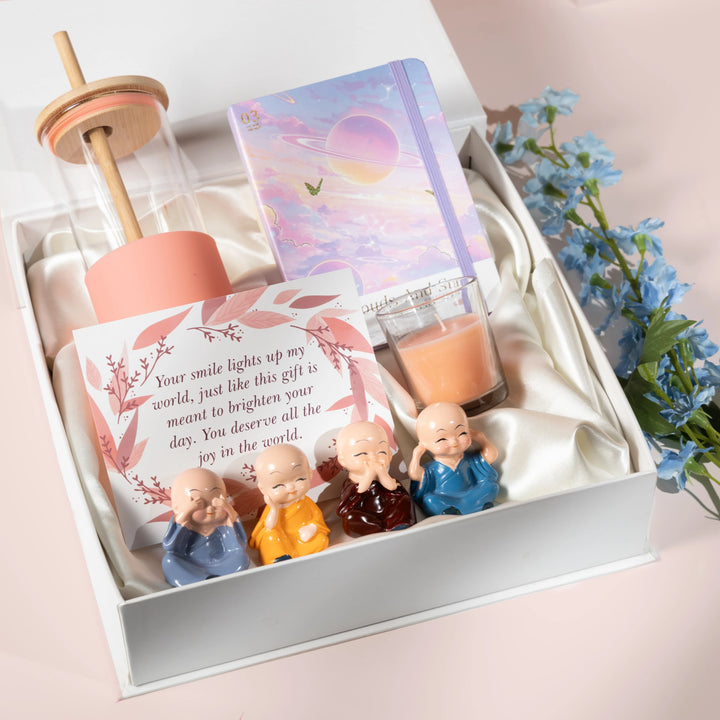 Rarejoy self-care gift hamper featuring a glass sipper bottle, aesthetic diary, scented candle, greeting card, and four monk figurines in a premium white gift box – perfect gift for women, friends, birthdays, and special occasions.