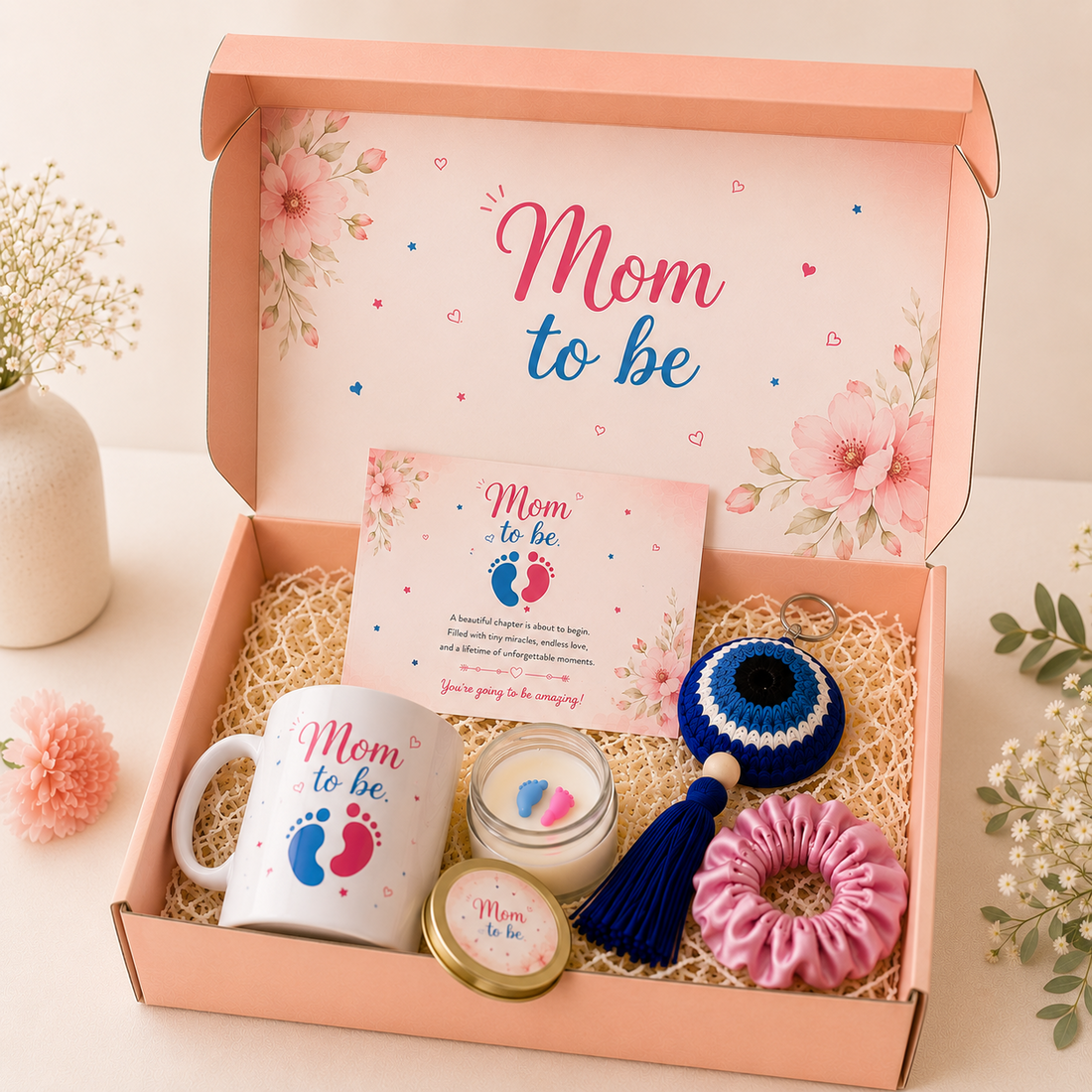 Luxury Mom To Be gift hamper featuring a personalized mug, scented candle, evil eye keychain, greeting card and satin scrunchie in a pastel pink gift box.