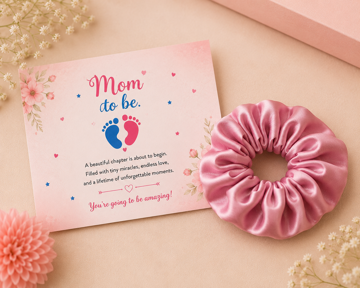 Baby shower greeting card with floral "Mom To Be" design paired with a pink satin scrunchie in a professional flat lay product photo.