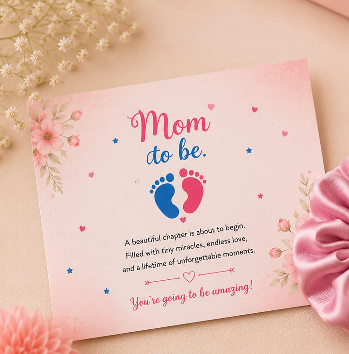 Baby shower greeting card with floral "Mom To Be" design paired with a pink satin scrunchie in a professional flat lay product photo.
