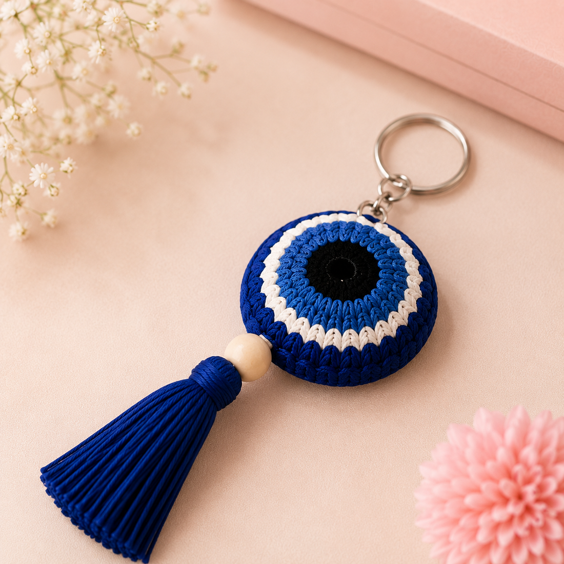 Handmade blue evil eye crochet keychain with tassel, displayed in a premium lifestyle product photography setting for gifting.