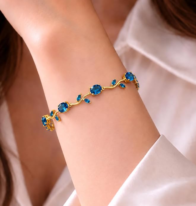 Rarejoy bracelet for women. A gold vine-style bracelet with blue gemstone accents worn on a woman's wrist, shown against a soft white blouse background.